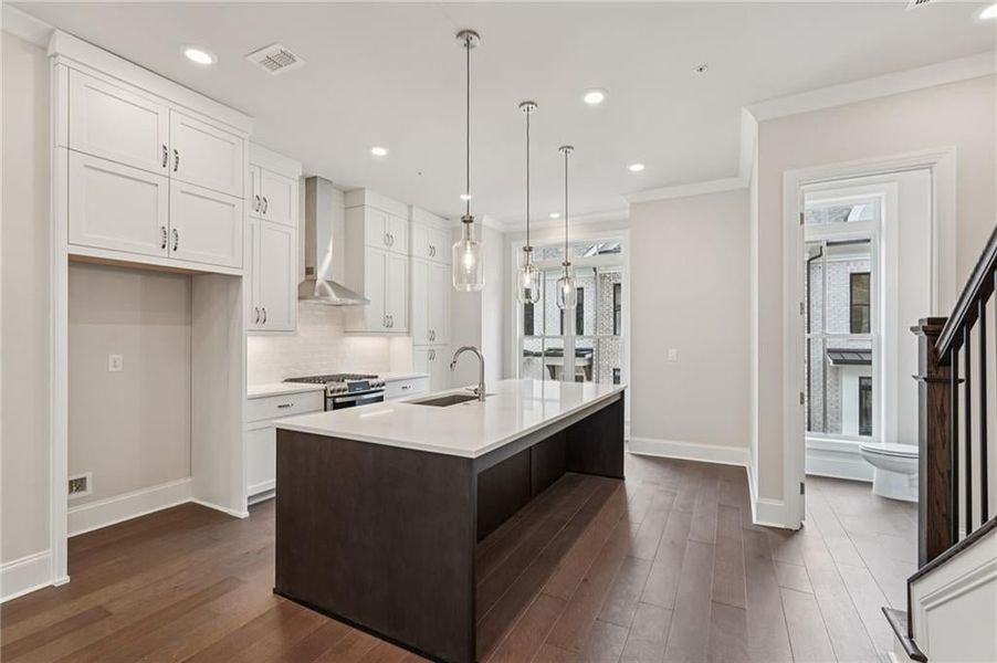 Dual tone kitchen with dark wood finished floors, dual tone cabinetry, pendant lighting, gas stove, and an island with sink