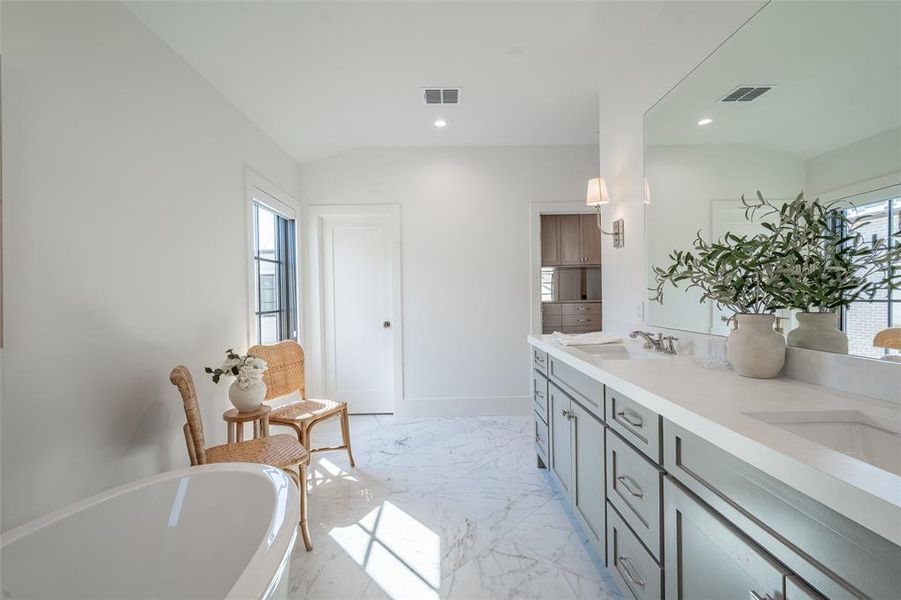 Primary bathroom featuring lofted ceiling, a tub to relax in, a wealth of natural light, and double vanity