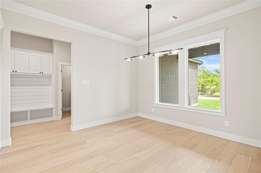 Unfurnished dining area with light wood-type flooring, crown molding, and a chandelier Unfurnished dining area with light wood-type flooring, crown molding, and a chandelier
