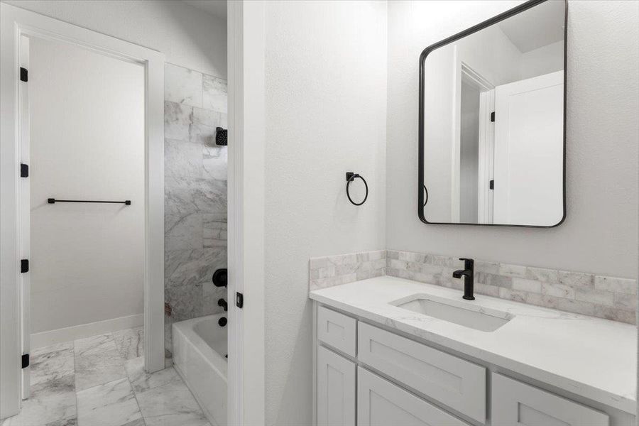 Bathroom with marble finish flooring, vanity, shower / bath combination, and baseboards Bathroom with marble finish flooring, vanity, shower / bath combination, and baseboards