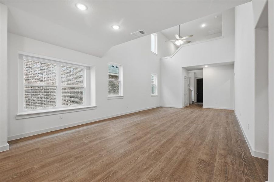 Unfurnished living room with high vaulted ceiling, baseboards, visible vents, a ceiling fan, and wood finished floors Unfurnished living room with high vaulted ceiling, baseboards, visible vents, a ceiling fan, and wood finished floors