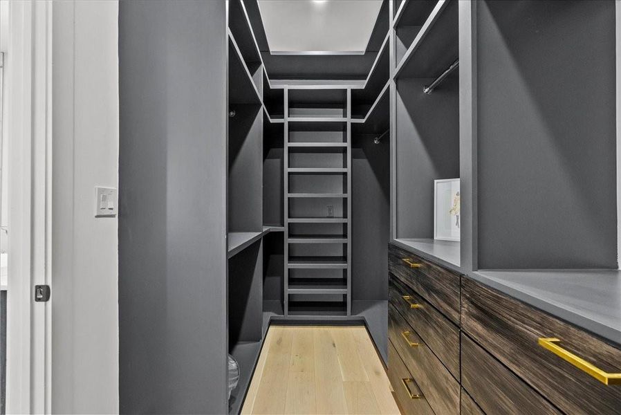 This is a spacious, modern walk-in closet featuring sleek gray shelving and cabinetry with gold handles. It offers ample storage, including multiple shelves, hanging spaces, and drawers, all set against a light wood floor. This is a spacious, modern walk-in closet featuring sleek gray shelving and cabinetry with gold handles. It offers ample storage, including multiple shelves, hanging spaces, and drawers, all set against a light wood floor.