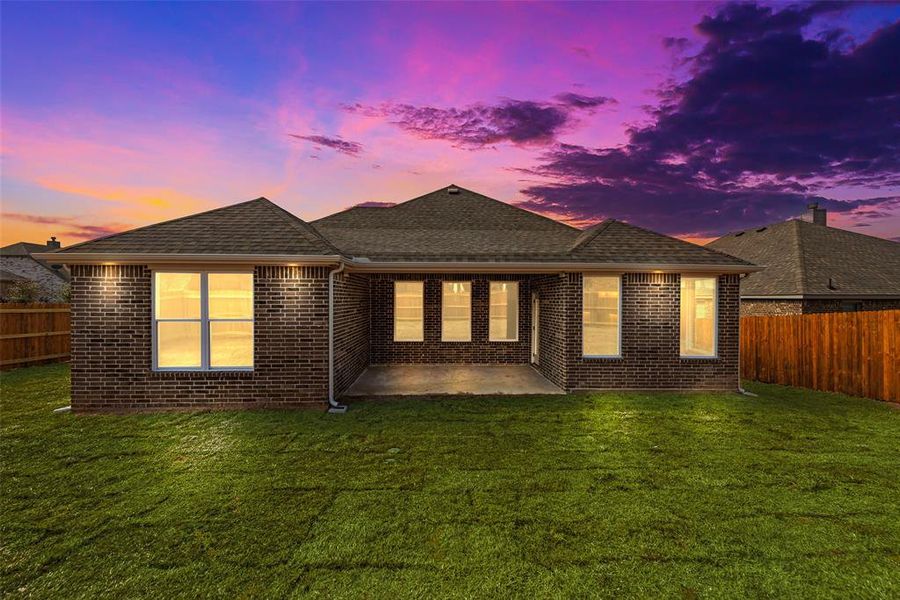 Back house at dusk with a patio and a lawn