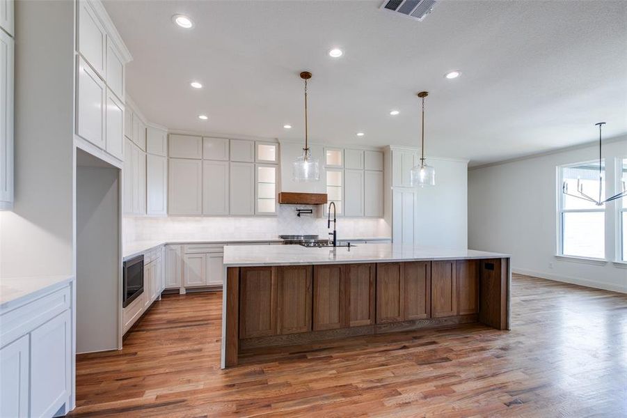 Kitchen with decorative backsplash, white cabinetry, hardwood / wood-style floors, and a kitchen island with sink