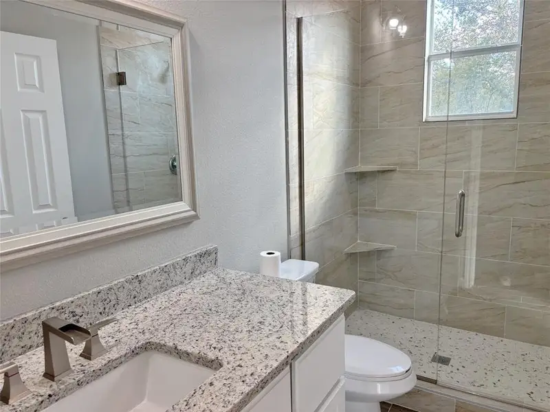 Bathroom with a textured wall, a shower stall, and vanity