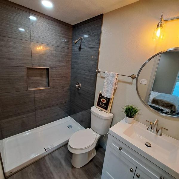 Bathroom featuring vanity, tiled shower, wood-type flooring, and toilet