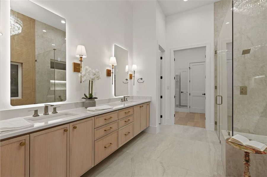 Bathroom featuring double vanity, a marble finish shower, and light marble finish flooring