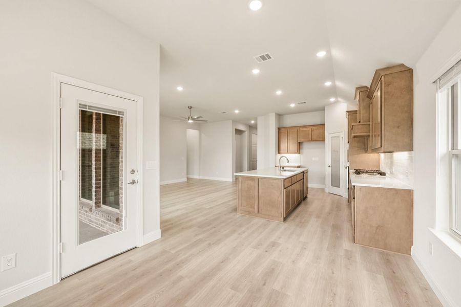 Open kitchen with wood cabinets, center island with sink, and light hardwood floors opening to living area Open kitchen with wood cabinets, center island with sink, and light hardwood floors opening to living area