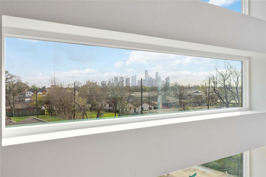 A sleek horizontal picture window captures a beautiful elevated view of the downtown Houston skyline and greenery, adding natural light and a scenic backdrop that enhances the home's modern architectural design.