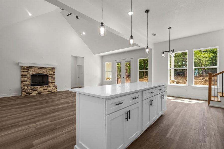 Open concept living area featuring vaulted ceilings, a brick-faced fireplace, and hardwood style flooring