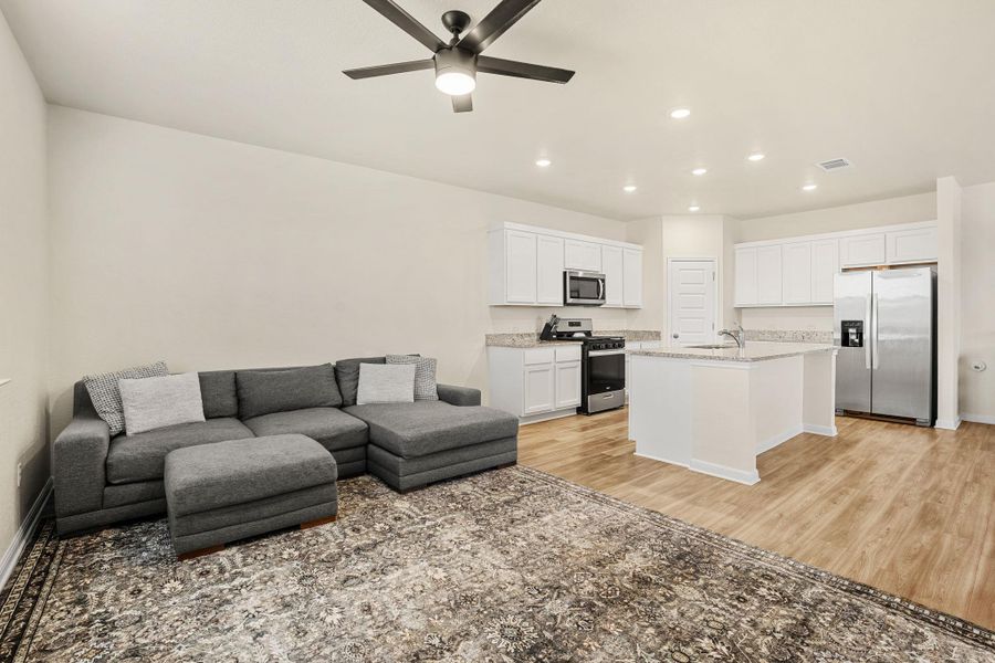 An open concept living area boasts a modern kitchen with ample counter space and a living room with a ceiling fan.