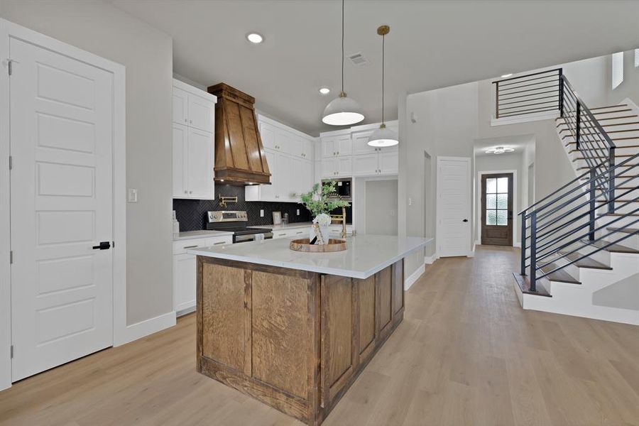 Kitchen featuring appliances with stainless steel finishes, light wood-style floors, premium range hood, baseboards, and backsplash Kitchen featuring appliances with stainless steel finishes, light wood-style floors, premium range hood, baseboards, and backsplash