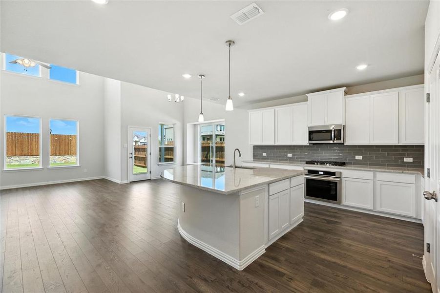 Kitchen featuring white cabinets, stainless steel appliances, hanging light fixtures, light stone countertops, and a high ceiling