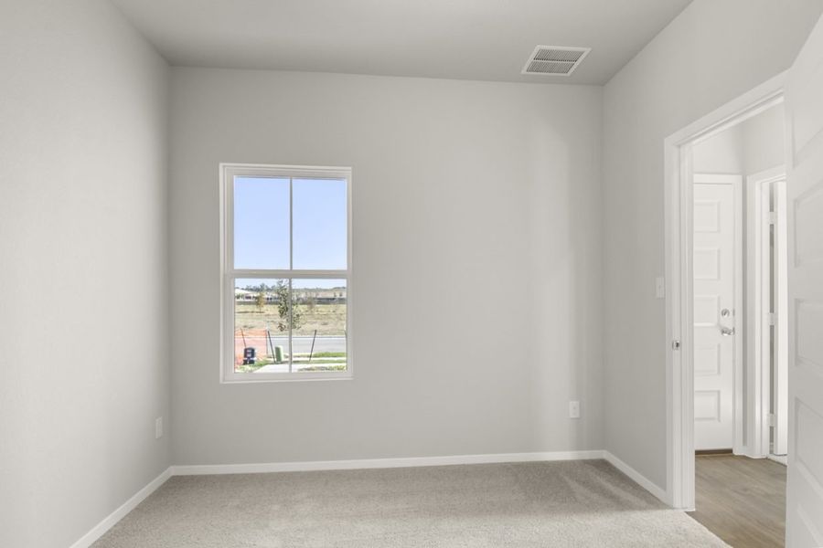 Image of a bedroom with tan carpeting, light grey walls and a window