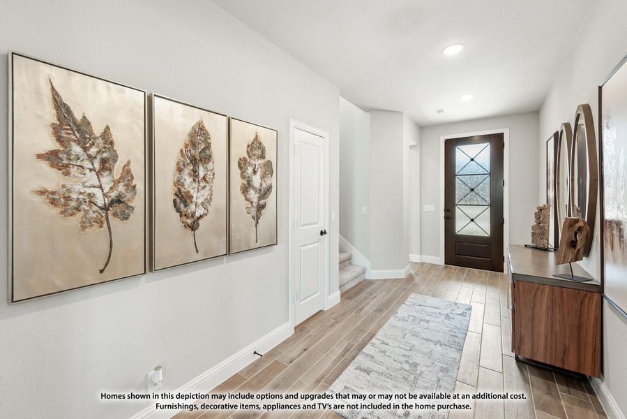Entryway with wood-look tile floors, dark front door, leaf artwork on wall, and console table with mirrors
