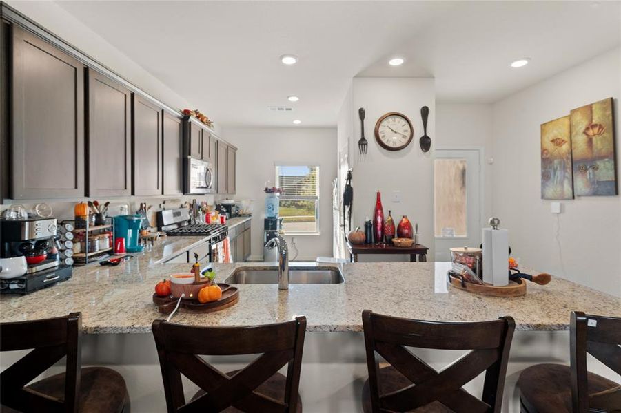 Kitchen with a kitchen breakfast bar, light stone countertops, appliances with stainless steel finishes, a peninsula, and recessed lighting