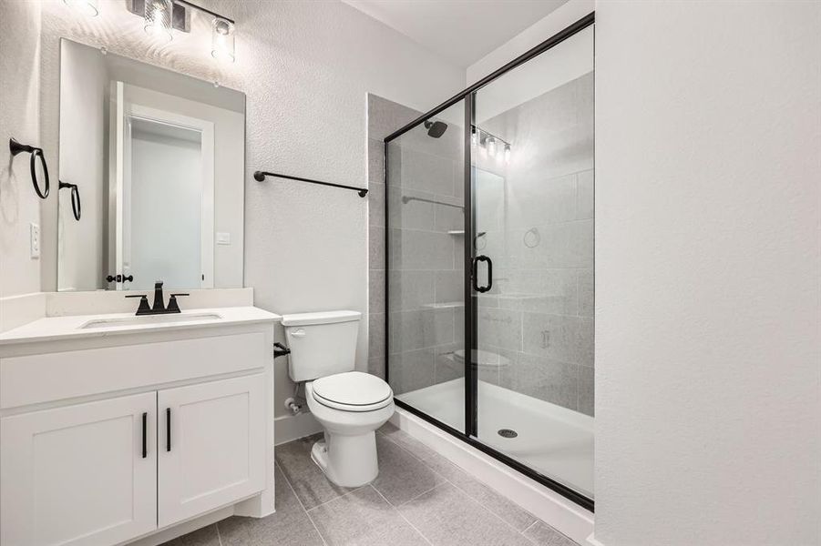 Bathroom featuring toilet, vanity, tile patterned floors, and a shower with shower door