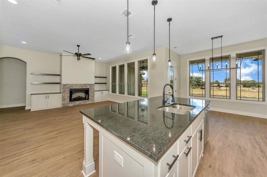 Kitchen featuring dark stone countertops, white cabinetry, sink, a stone fireplace, and a center island with sink