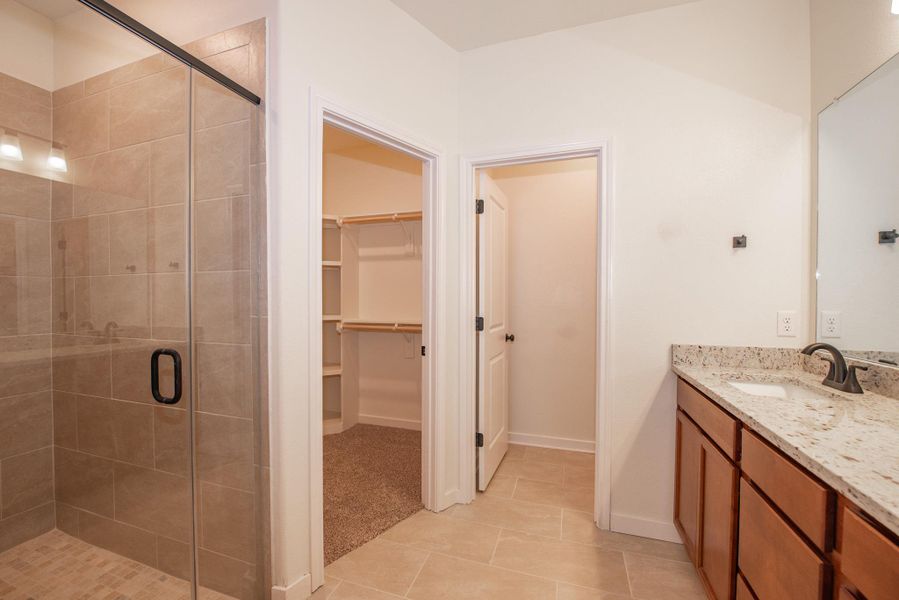 Full bath featuring a stall shower, vanity, light tile patterned floors, and a spacious closet