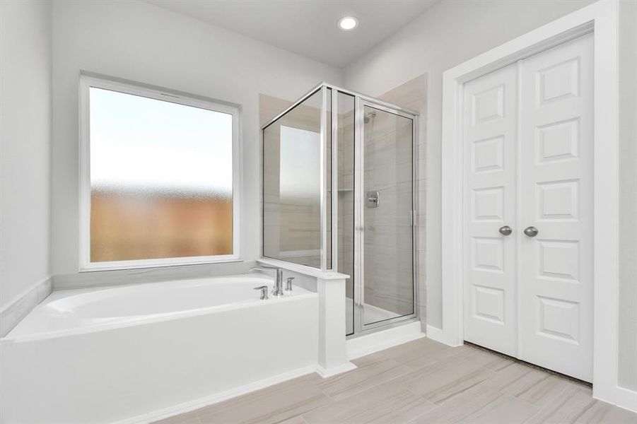 The primary en-suite has a soaking tub to give you that spa experience. The large privacy window allow lots of nature light in the space.  Sample photo of completed home with similar plan. As built color and selections may vary.