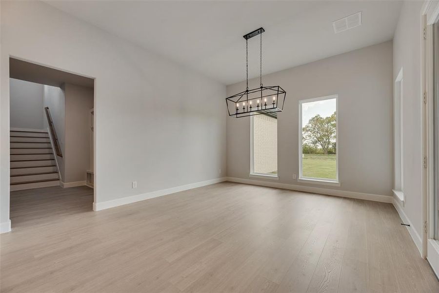 Unfurnished dining area featuring stairs, light wood finished floors, and a chandelier