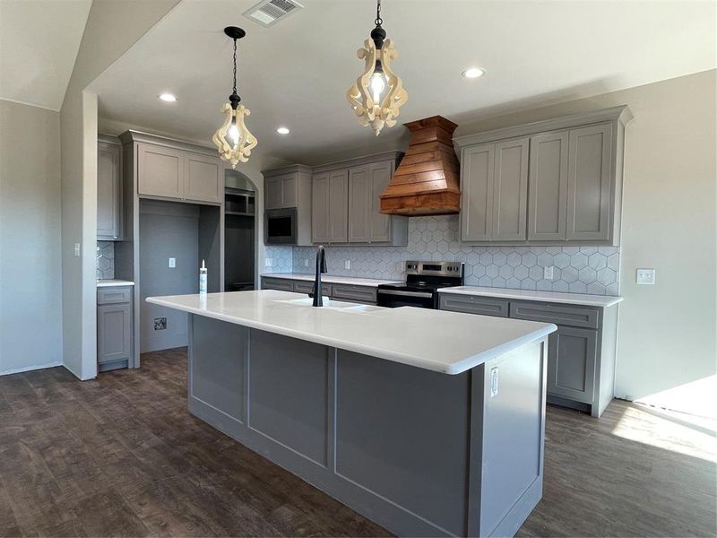 Kitchen featuring stove, backsplash, exhaust hood, dark wood-type flooring, and decorative light fixtures