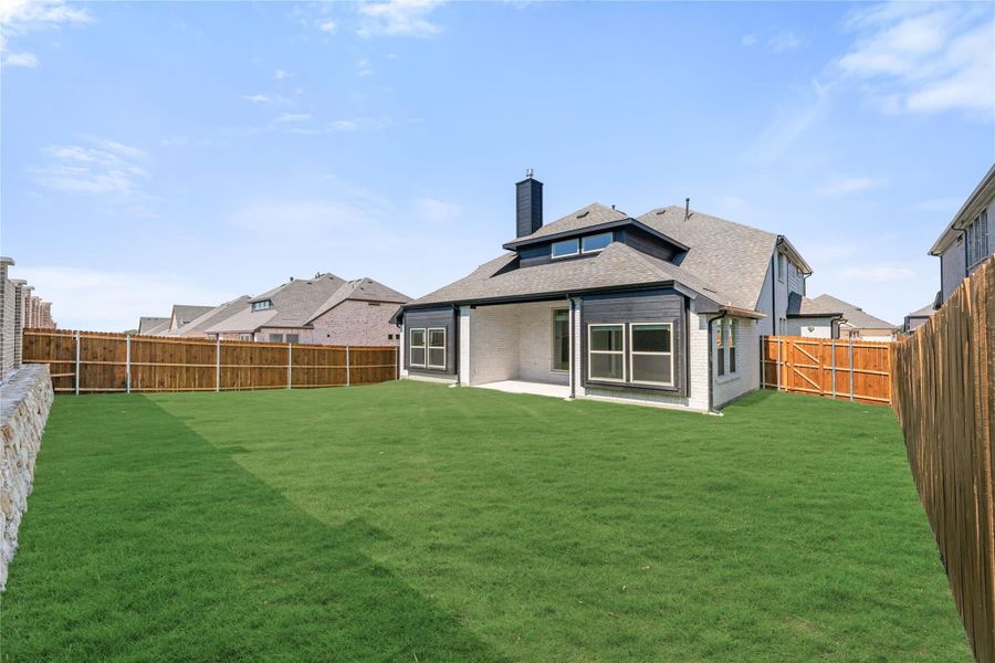 Backyard of two-story home with large green lawn, covered patio, and wood privacy fence