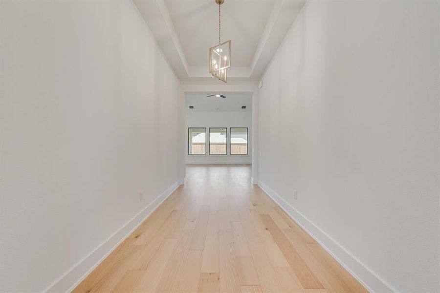Corridor featuring light wood finished floors, a chandelier, and a tray ceiling