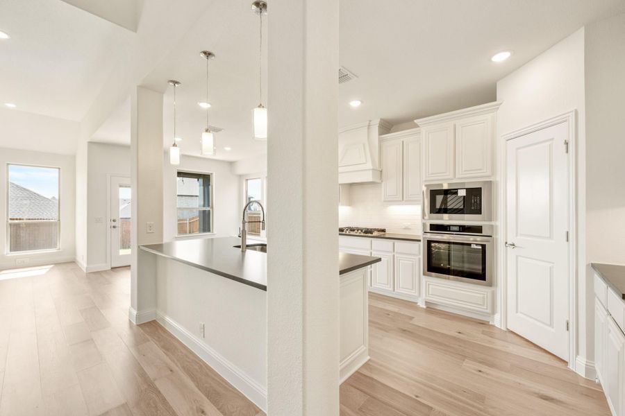 Kitchen with white cabinets, dark countertops, stainless steel appliances, center island with sink, and light hardwood floors Kitchen with white cabinets, dark countertops, stainless steel appliances, center island with sink, and light hardwood floors