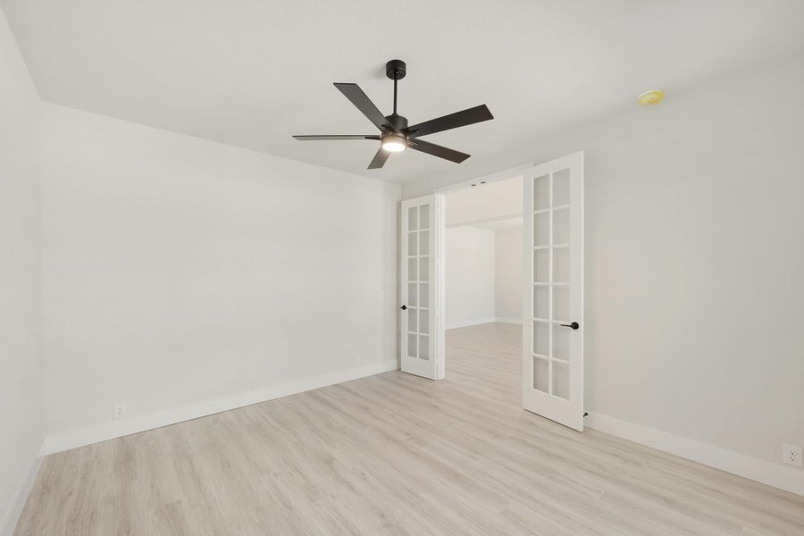 Empty room with light wood floors, ceiling fan, and white French doors opening to adjacent space