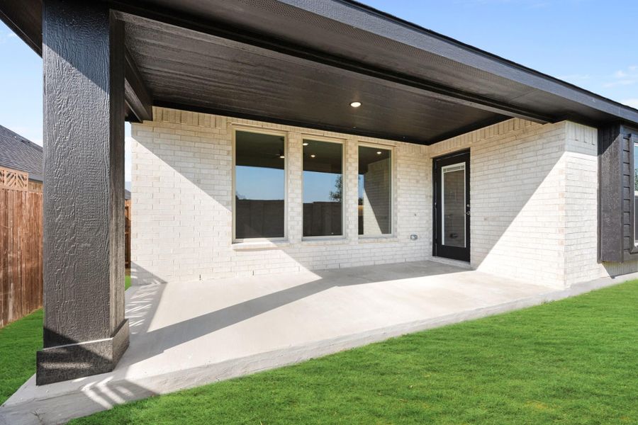 Covered back patio with concrete floor, white brick exterior, large windows, and black door overlooking green lawn Covered back patio with concrete floor, white brick exterior, large windows, and black door overlooking green lawn