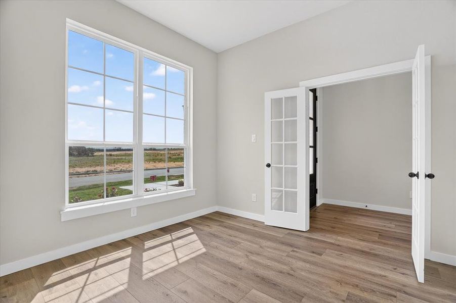 Room featuring wood-finish flooring, a large multi-pane window with white trim, and a pair of French doors with black hardware