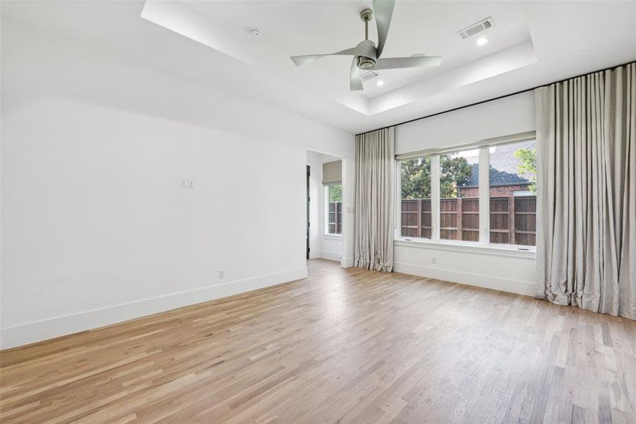 Spare room with ceiling fan, light hardwood / wood-style flooring, and a tray ceiling