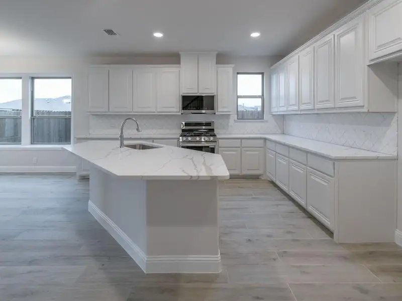 Kitchen with light stone countertops, sink, backsplash, white cabinets, and appliances with stainless steel finishes