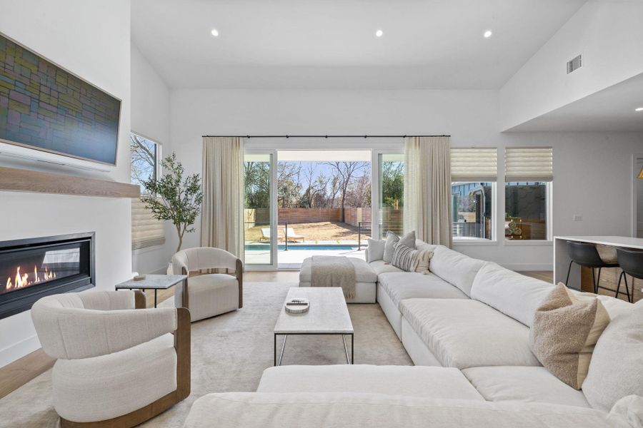 Living room with recessed lighting, wood finished floors, a glass covered fireplace, and vaulted ceiling