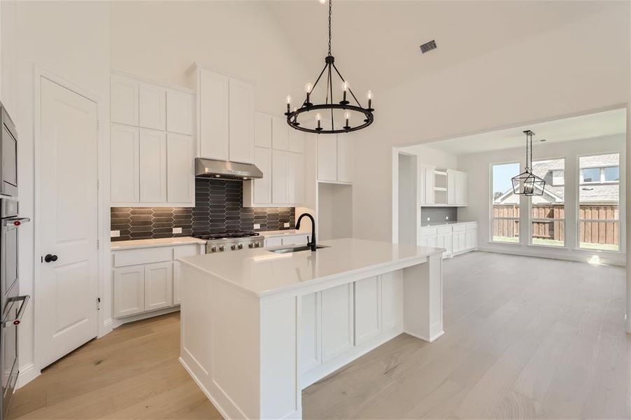 Kitchen featuring tasteful backsplash, a kitchen island with sink, white cabinetry, light wood-type flooring, and sink