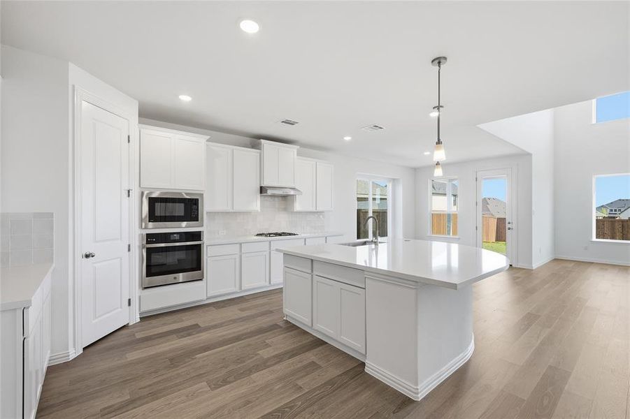 Kitchen with stainless steel appliances, a center island with sink, white cabinetry, and decorative light fixtures