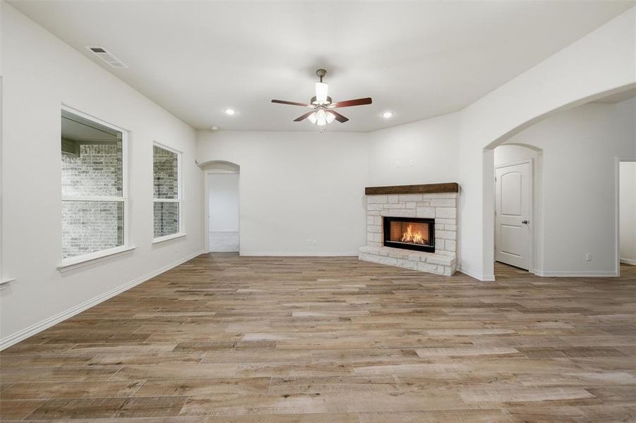 Unfurnished living room featuring arched walkways, a ceiling fan, a fireplace, light wood-type flooring, and recessed lighting