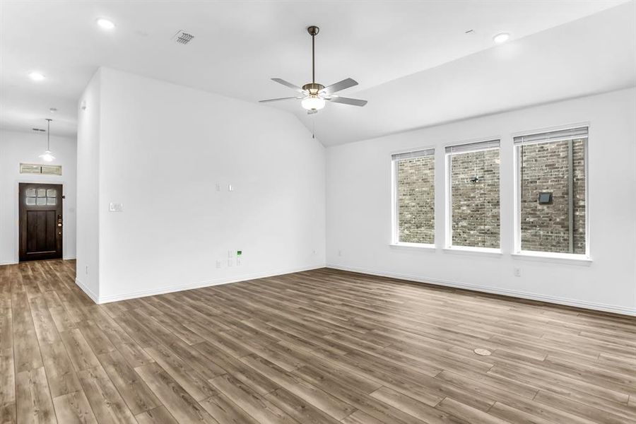 Spacious living area featuring wood-finish flooring, vaulted ceilings, and a ceiling fan