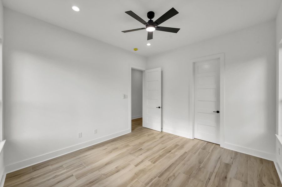 Another view of the spacious bedroom highlighting neutral finishes, recessed lighting, and easy access to hallway and closet space.