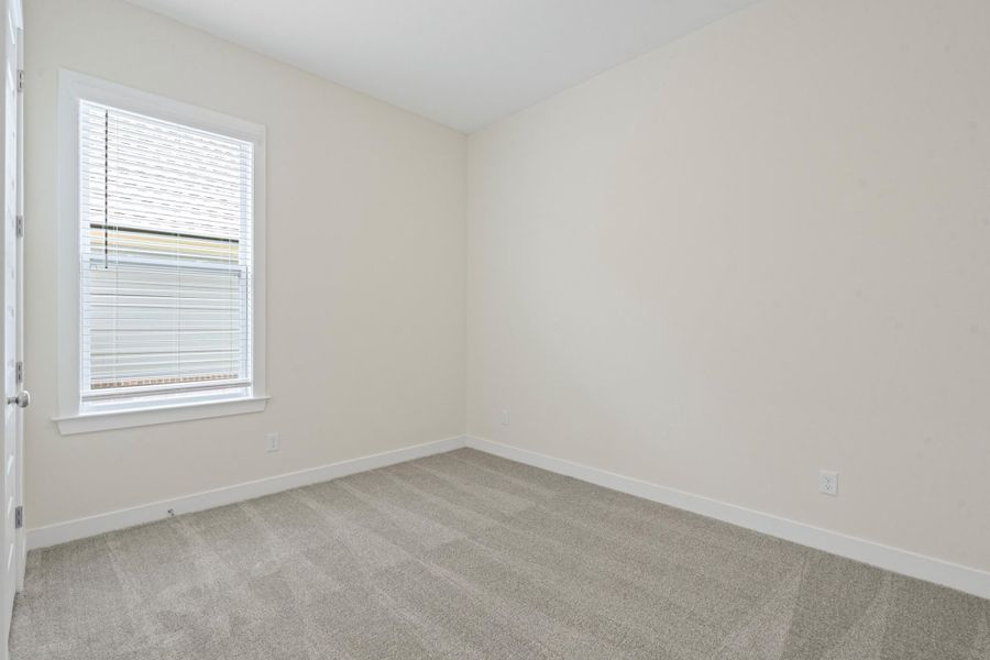 Neutral-toned room featuring a single window with blinds, light-colored walls, and gray patterned carpeting Neutral-toned room featuring a single window with blinds, light-colored walls, and gray patterned carpeting