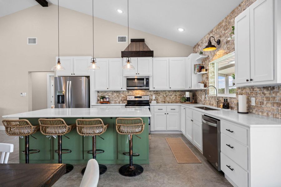 Kitchen featuring a center island, two tone cabinetry, stainless steel appliances, a breakfast bar area, and vaulted ceiling