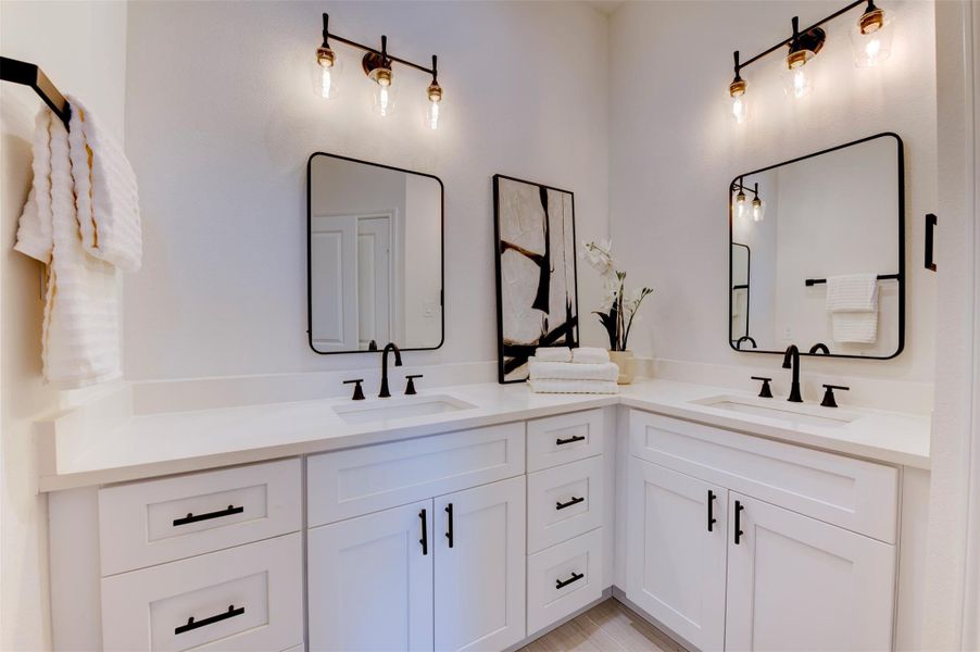 Dual-sink primary bath vanity with white shaker cabinets, quartz countertop, matte black hardware, black-framed mirrors, and Edison-style sconce lighting on both sides.