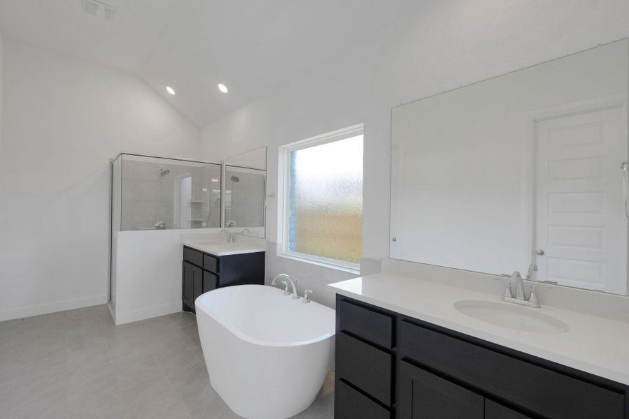 Full bathroom with two vanities, a stall shower, lofted ceiling, a freestanding tub, and recessed lighting