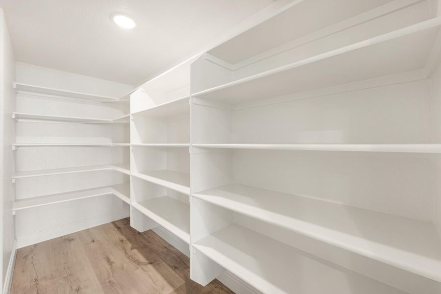 Walk-in pantry with white built-in shelves on three walls and light wood floors