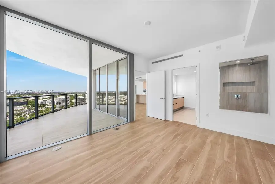 Floor-to-ceiling glass panel doors, expansive covered balcony, wood-finish flooring, and built-in glass-enclosed shower featuring stone-finish wall tile and recessed shelving Floor-to-ceiling glass panel doors, expansive covered balcony, wood-finish flooring, and built-in glass-enclosed shower featuring stone-finish wall tile and recessed shelving