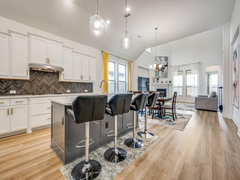 Kitchen featuring decorative backsplash, light wood-style flooring, gas cooktop, under cabinet range hood, and open floor plan