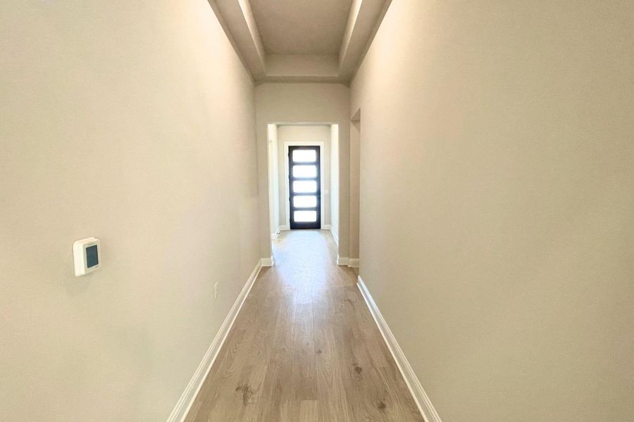 A long hallway features recessed tray ceilings and durable wood flooring leading to the entrance. A long hallway features recessed tray ceilings and durable wood flooring leading to the entrance.