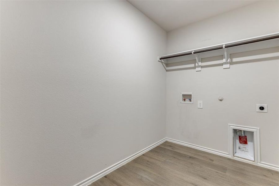 Laundry room featuring wood-finish flooring, white walls, white baseboards, and a clothing rod with shelf supports Laundry room featuring wood-finish flooring, white walls, white baseboards, and a clothing rod with shelf supports
