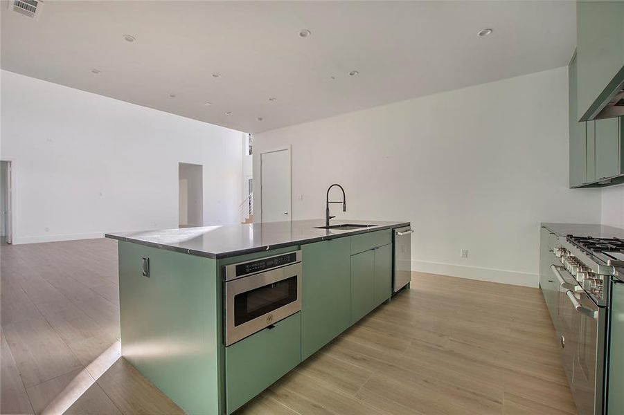 Kitchen featuring light hardwood / wood-style floors, a center island with sink, stainless steel appliances, green cabinetry, and sink